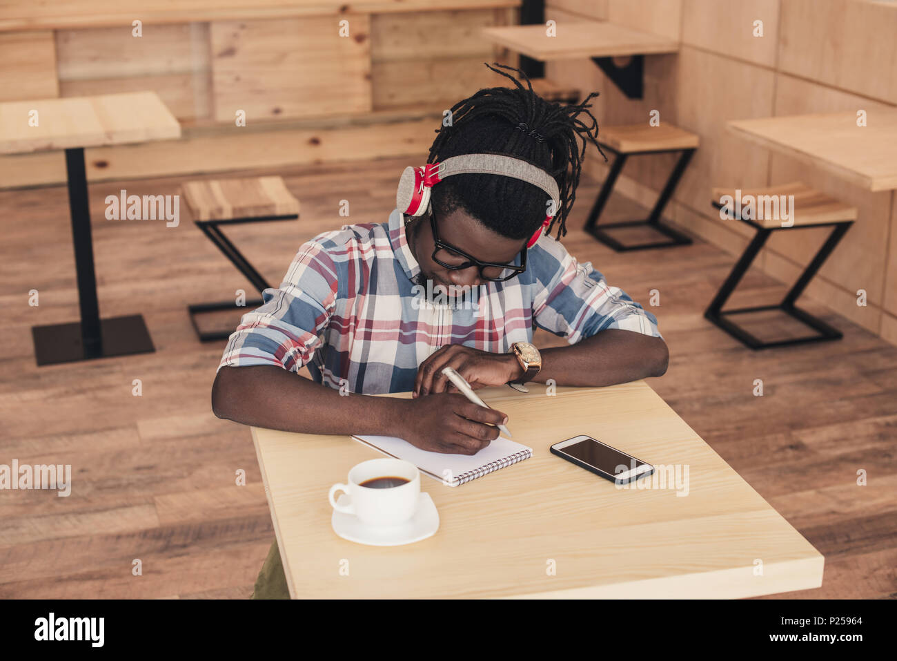 african american man listening music and writing in notepad in coffee ...