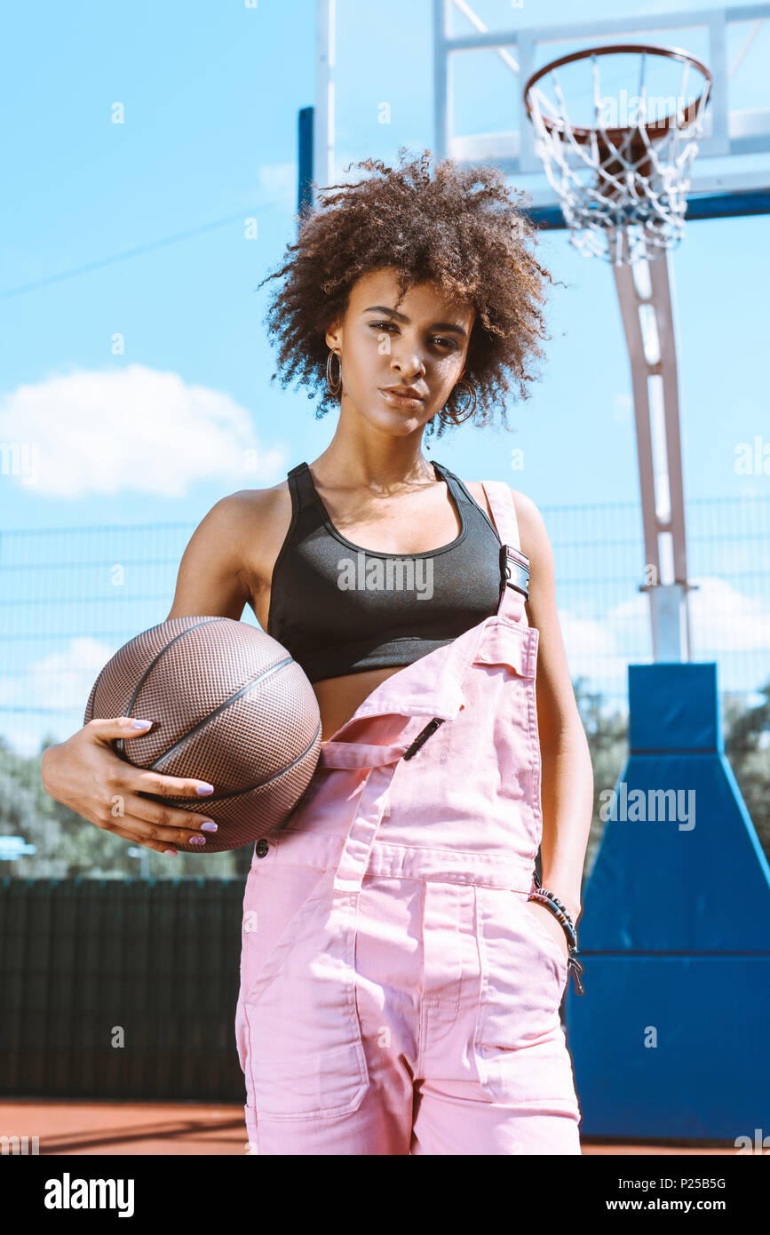 young africanamerican woman in sports bra and pink overalls holding a