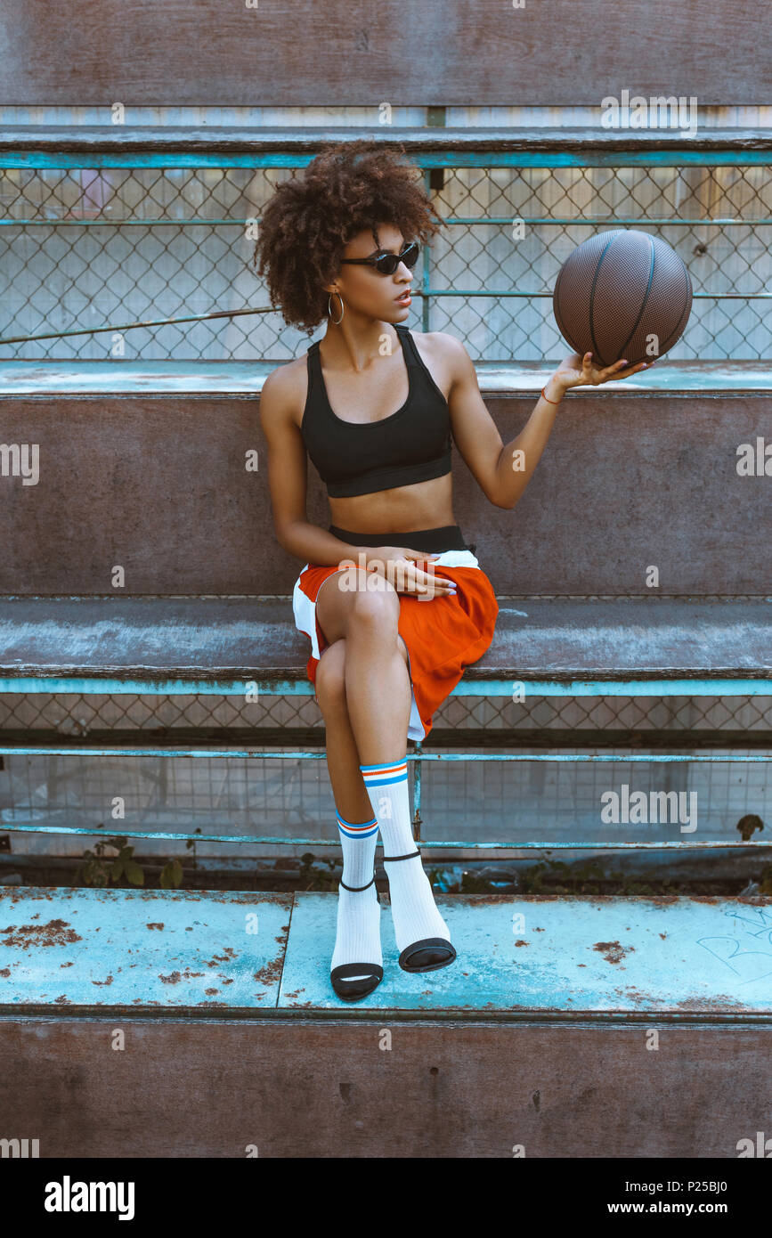 Young african-american woman in sportive attire and high heels sitting on  bench with basketball ball in her hand Stock Photo - Alamy