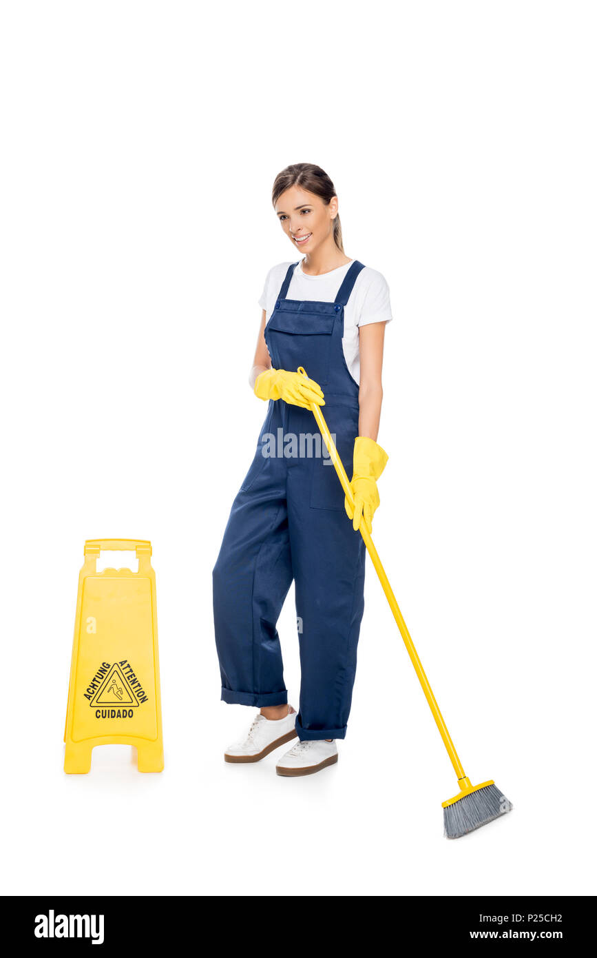 smiling cleaner in uniform with broom in hands looking away isolated on white Stock Photo