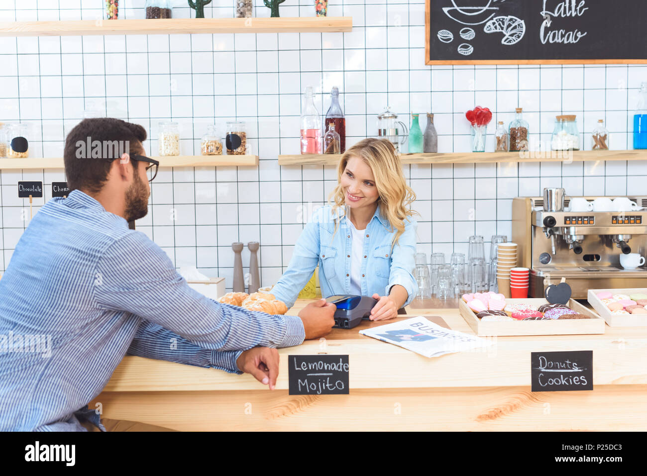 smiling young waitress with payment terminal looking at client in cafe ...
