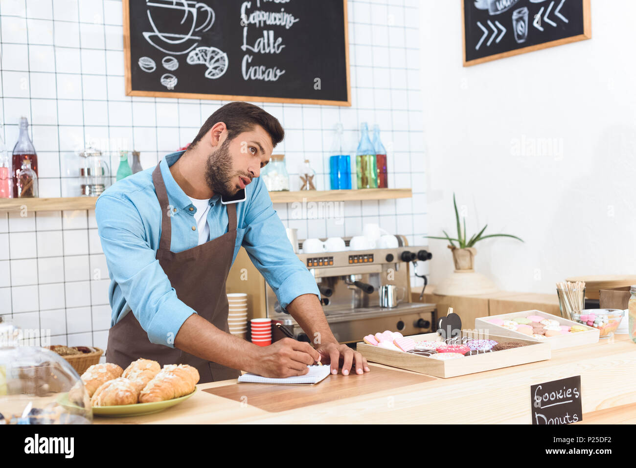 confident young cafe owner taking notes and talking on smartphone Stock Photo