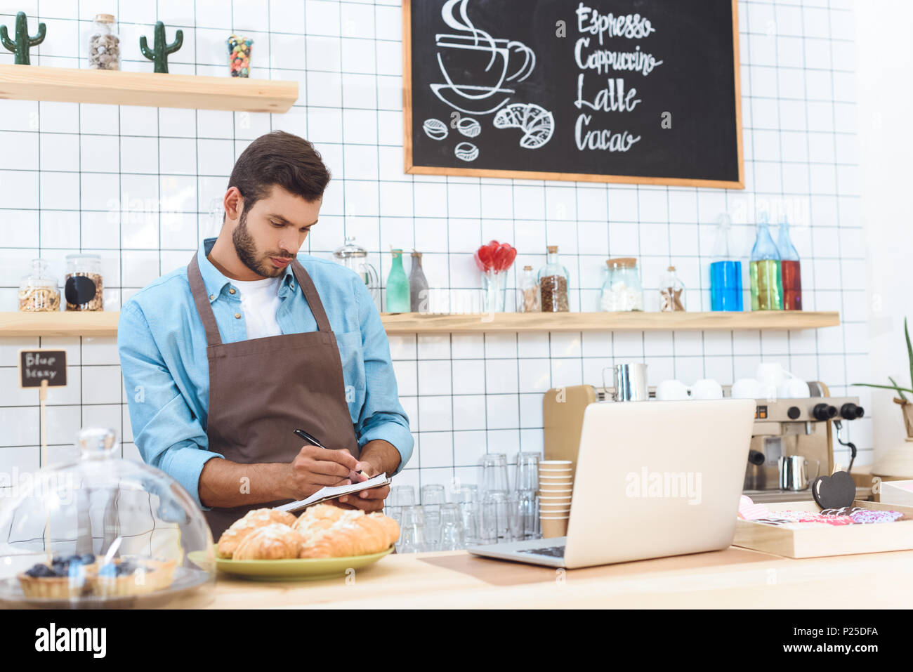 confident young cafe owner taking notes and working with laptop Stock Photo