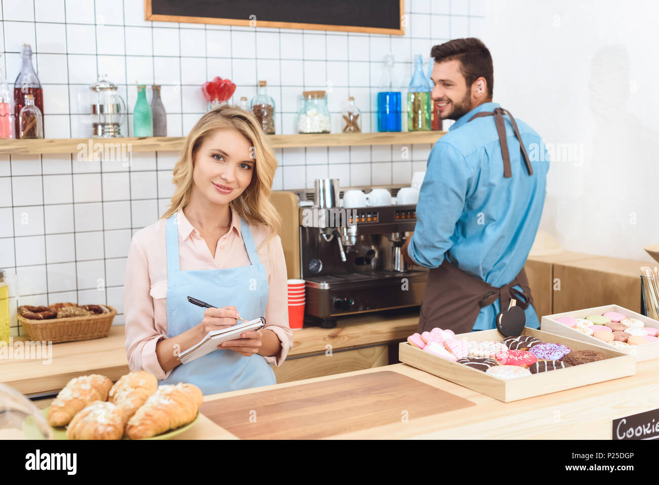 beautiful young waitress taking notes and smiling at camera while ...