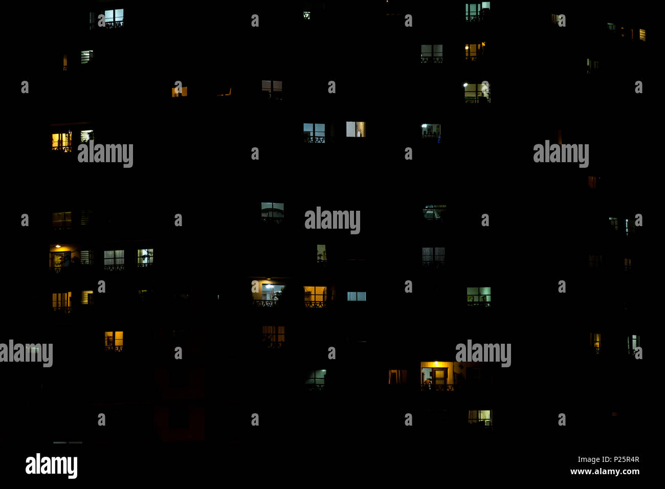 multiple windows of an apartment building at night. Some yellow, some blue, some light on, some light off. Stock Photo