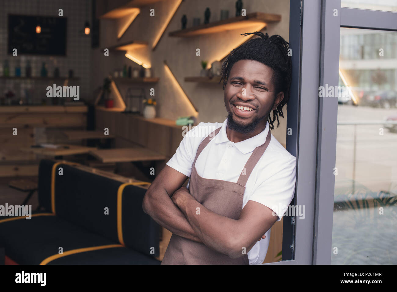 cheerful african american cafe owner in apron standing at entrance Stock Photo