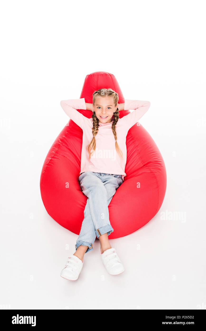 Young happy child resting on a red bean bag with arms behind head ...