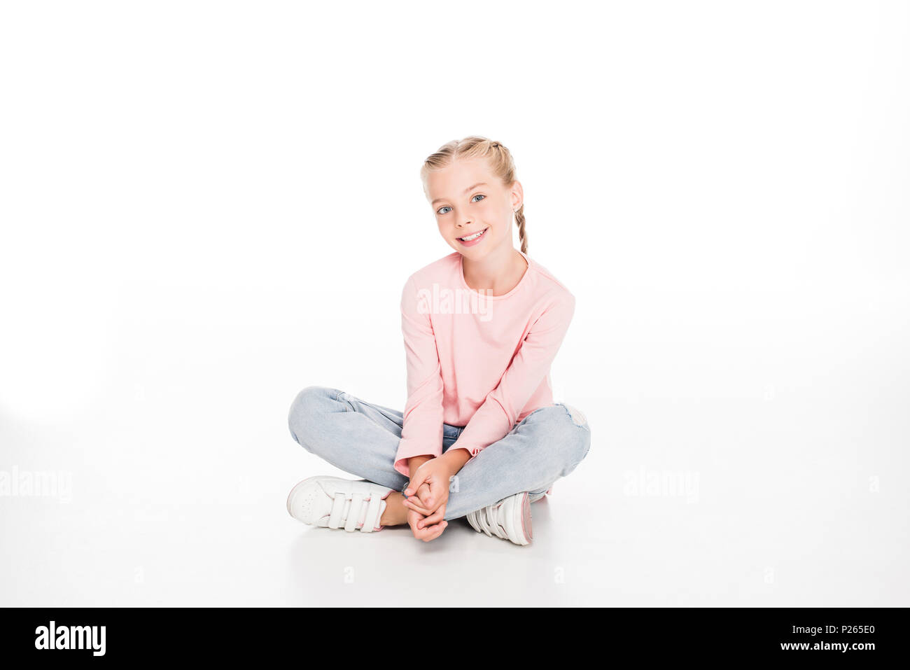 Cheerful child sitting on floor with legs crossed, isolated on white ...
