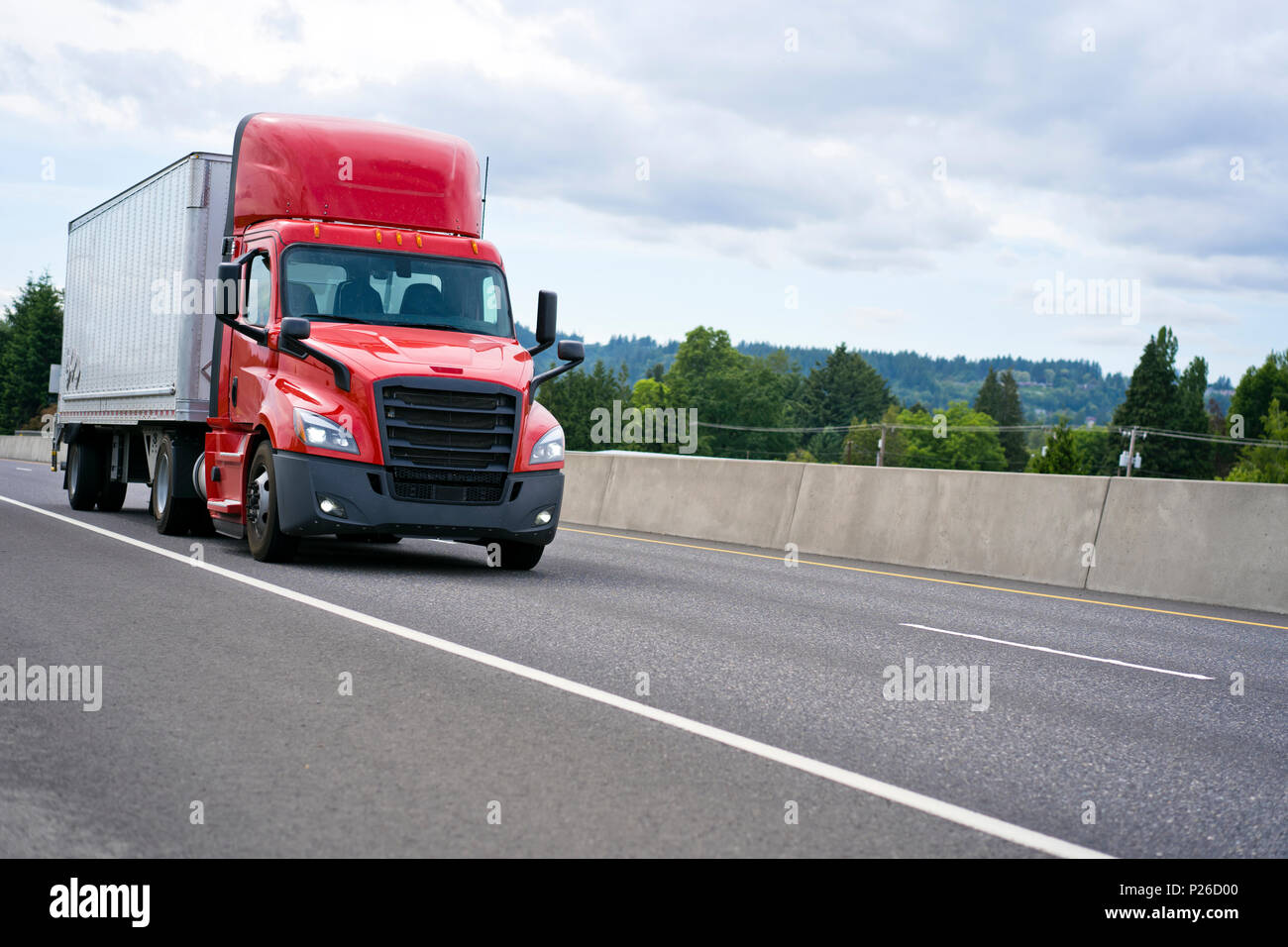 Commercial big rig red day cab local haul semi truck with roof spoiler transporting dry van semi trailer on the highway road for delivery of industria Stock Photo