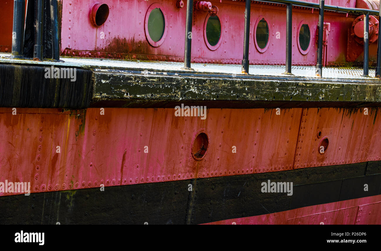 Portholes and deck on an old red rusty boat with a black stripe Stock Photo