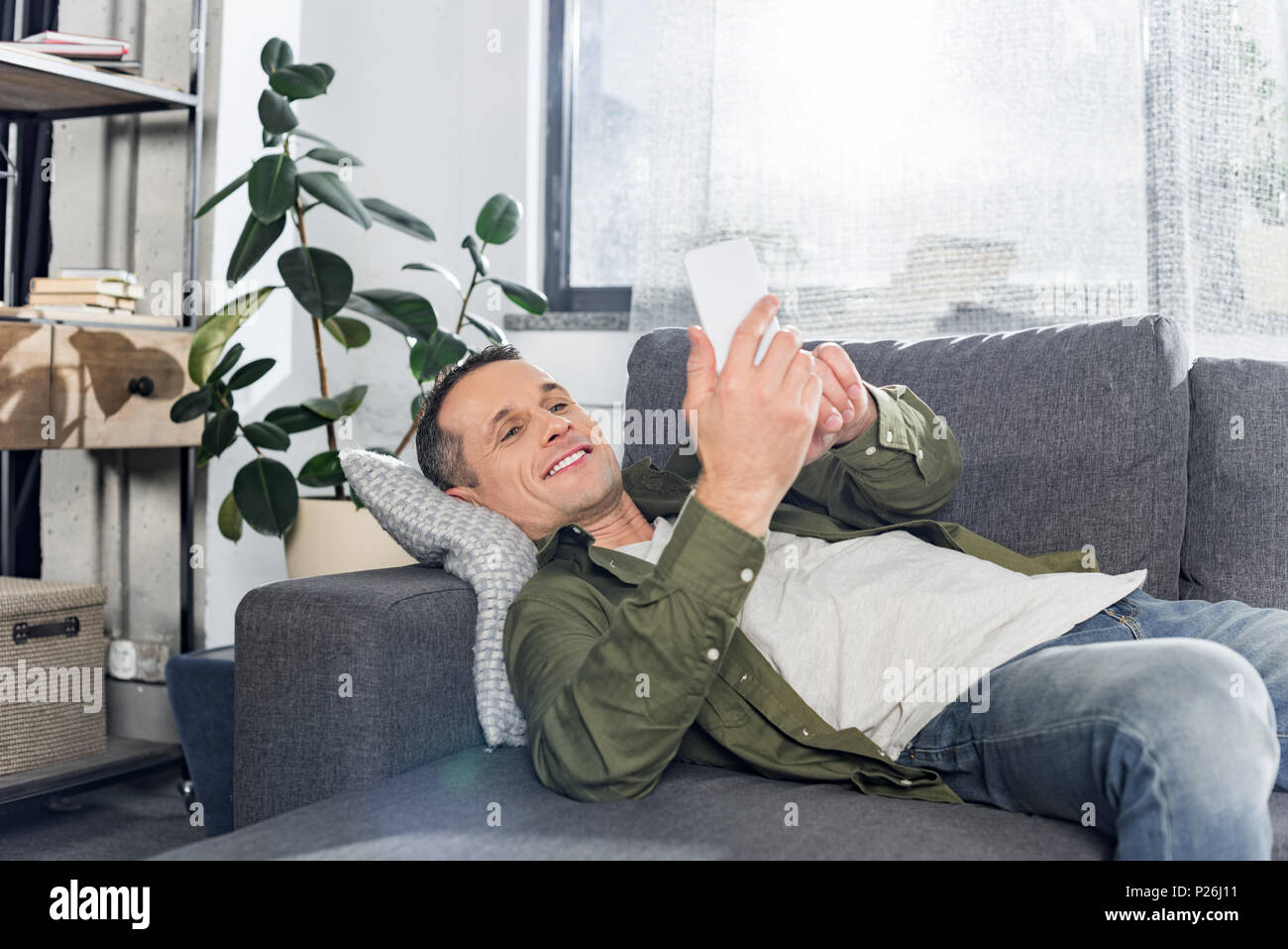 man using smartphone while laying on couch Stock Photo