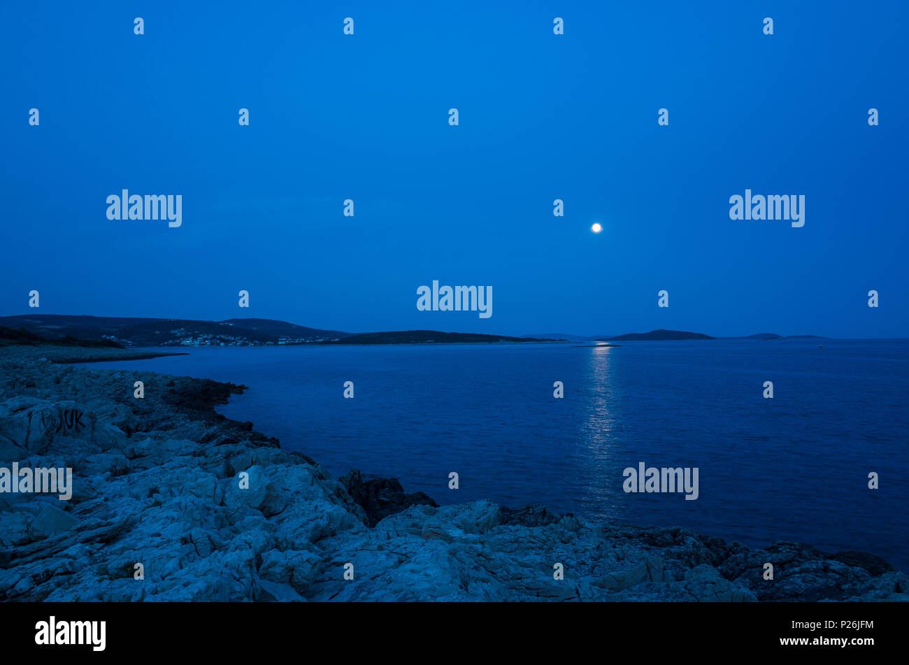 Beautiful night photo of Adriatic Sea in Croatia. Nice blue colors and moon in sky. Rock and stone beach. Calm, peaceful background image. Stillness a Stock Photo