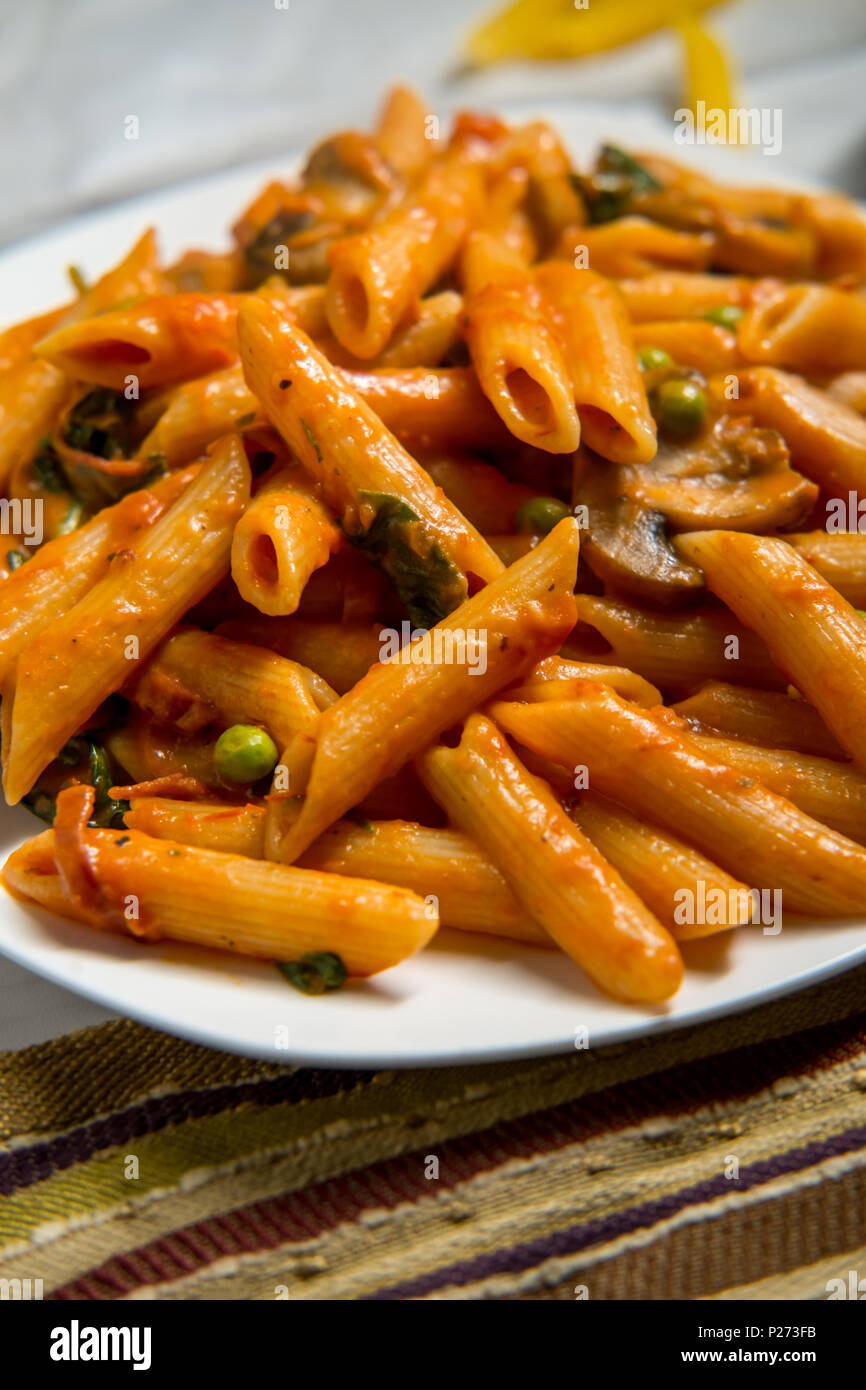 Penne pasta in creamy vodka tomato sauce with mushrooms peas and