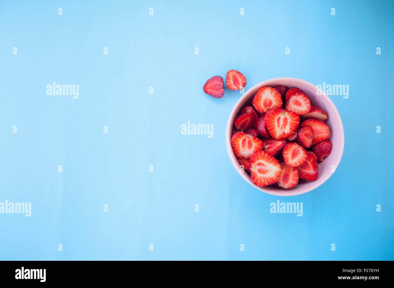 A pink bowl full of beautiful fresh juicy strawberries on bright blue ...