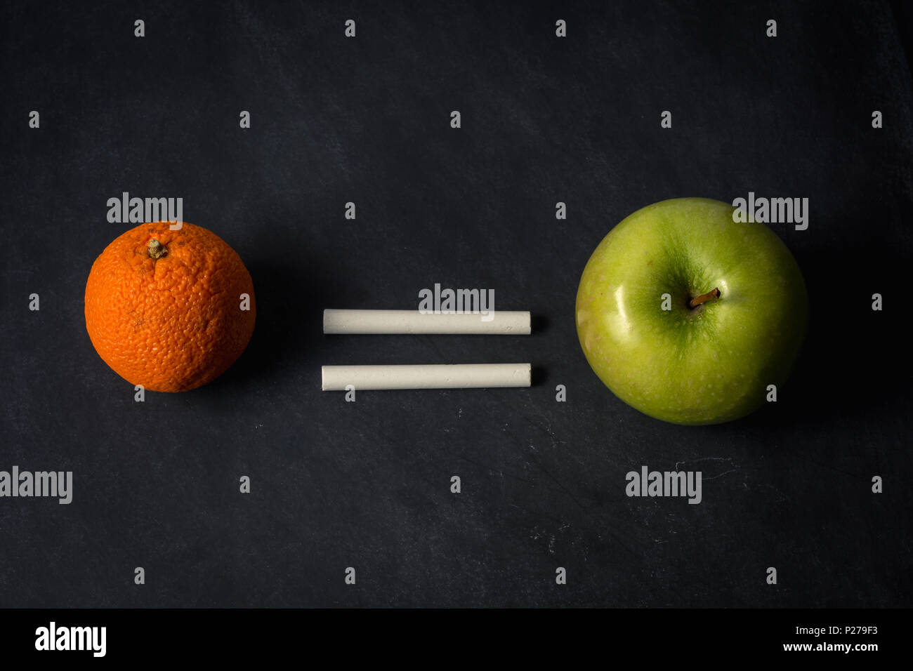 Orange equals apple with chalk on top of chalkboard suggesting equality in different fruit Stock Photo
