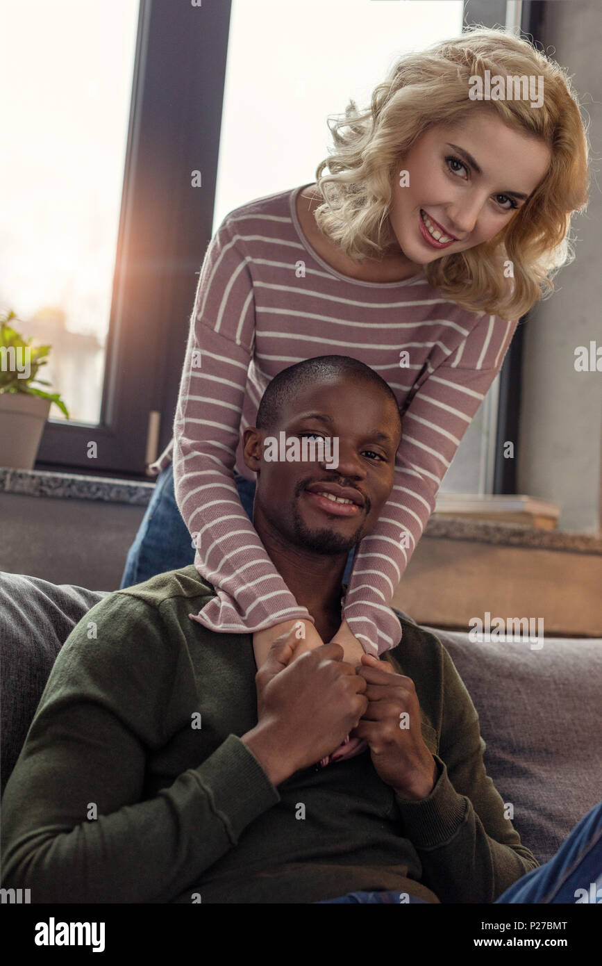 smiling caucasian woman hugging african american boyfriend on sofa at ...