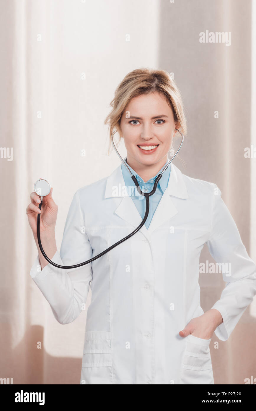 portrait of smiling female doctor in white coat showing stethoscope in ...