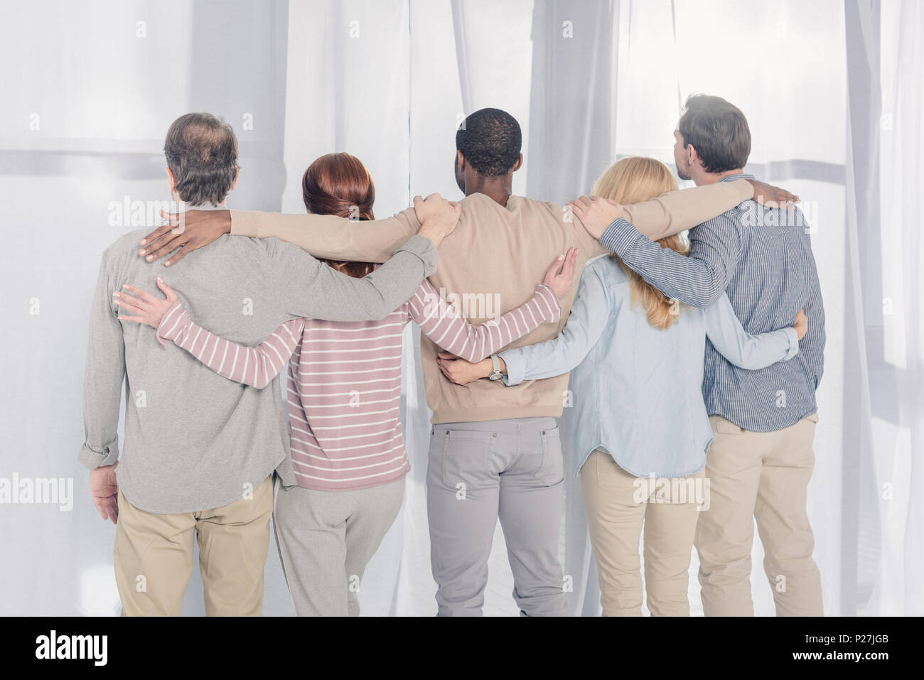 rear view of multiethnic people standing and embracing during group ...
