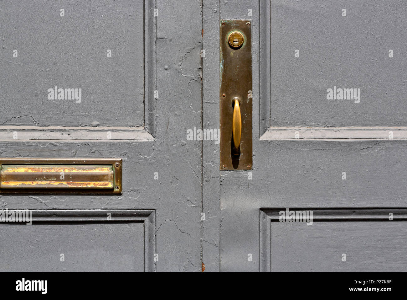 Close up of an Entry Door on a Cast Iron Building, Gray Paint, Wood Paneled, Old Brass Door Knob and Lock, Mail Slot.  Soho, Manhattan, New York City. Stock Photo