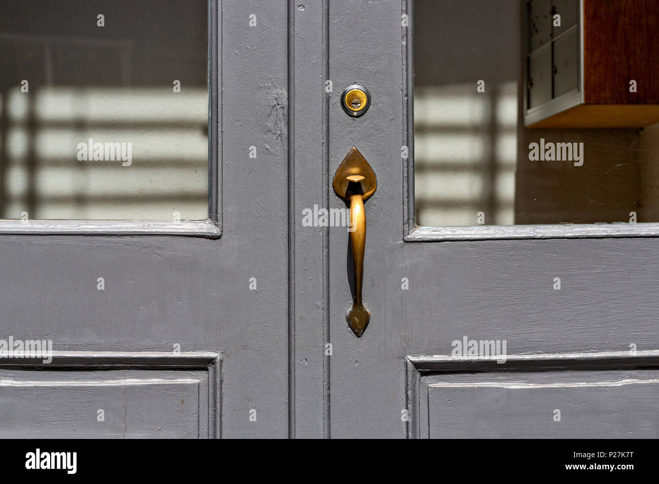 Close up of an Entry Door on a Cast Iron Building, Gray Paint, Wood Paneled, Old Brass Door Knob and Lock, Windows, Sun Shadows..  Soho, Manhattan, Ne Stock Photo