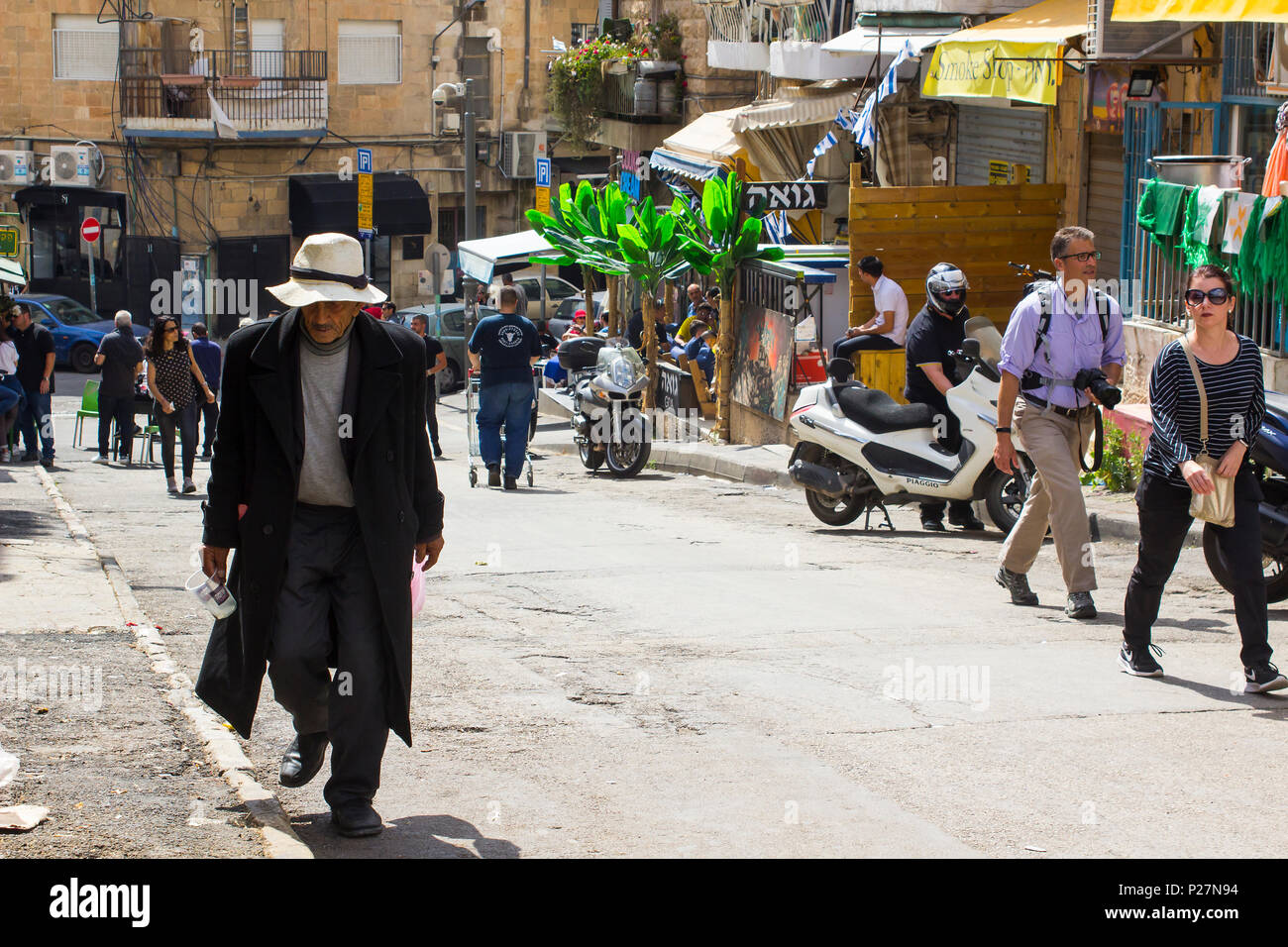 9 May 2018 An aged man in a long dark coat and floppy hat making his way up a hill at the busy Mahane Yehuda street market in Jerusalem Israel Stock Photo