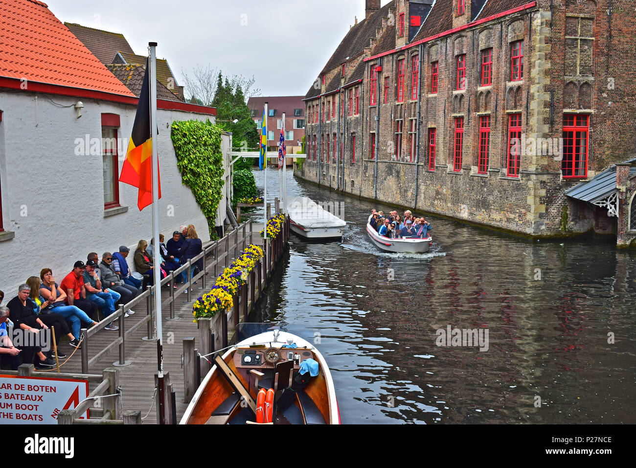 Passengers waiting patiently for the arrival of a canal boat for a tour of the city centre waterways of Bruges or Brugge, Belgium Stock Photo