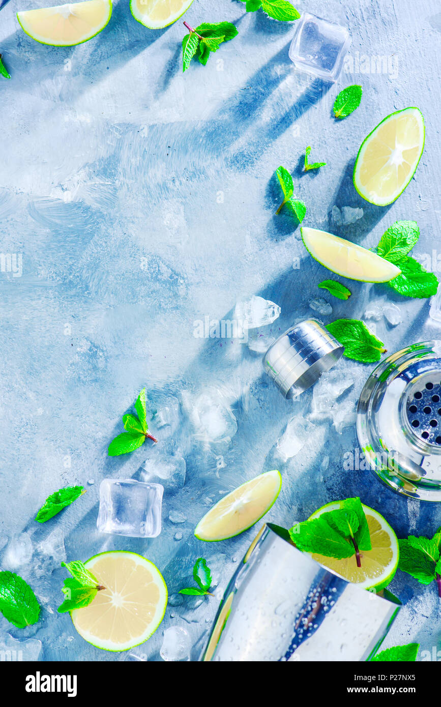 Fresh mojito cocktail ingredients, mint, lime and ice cubes on a gray stone background. Shaker and bar accessories flat lay. Summer drink concept with Stock Photo