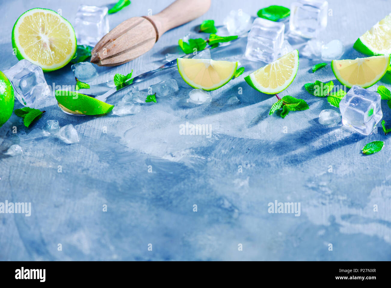 Summer drink header with mojito cocktail ingredients, mint, lime and ice cubes. Lemon reamer or juicer on a gray stone background with copy space. Stock Photo