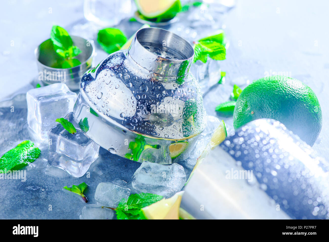 Shaker and bar accessories close-up. Mojito cocktail ingredients, mint, lime and ice cubes on a gray stone background. Summer drink concept with copy  Stock Photo