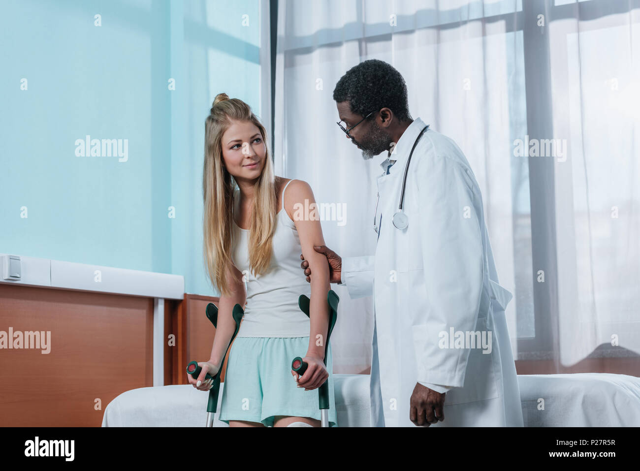 african american Doctor helping patient with leg brace and crutches