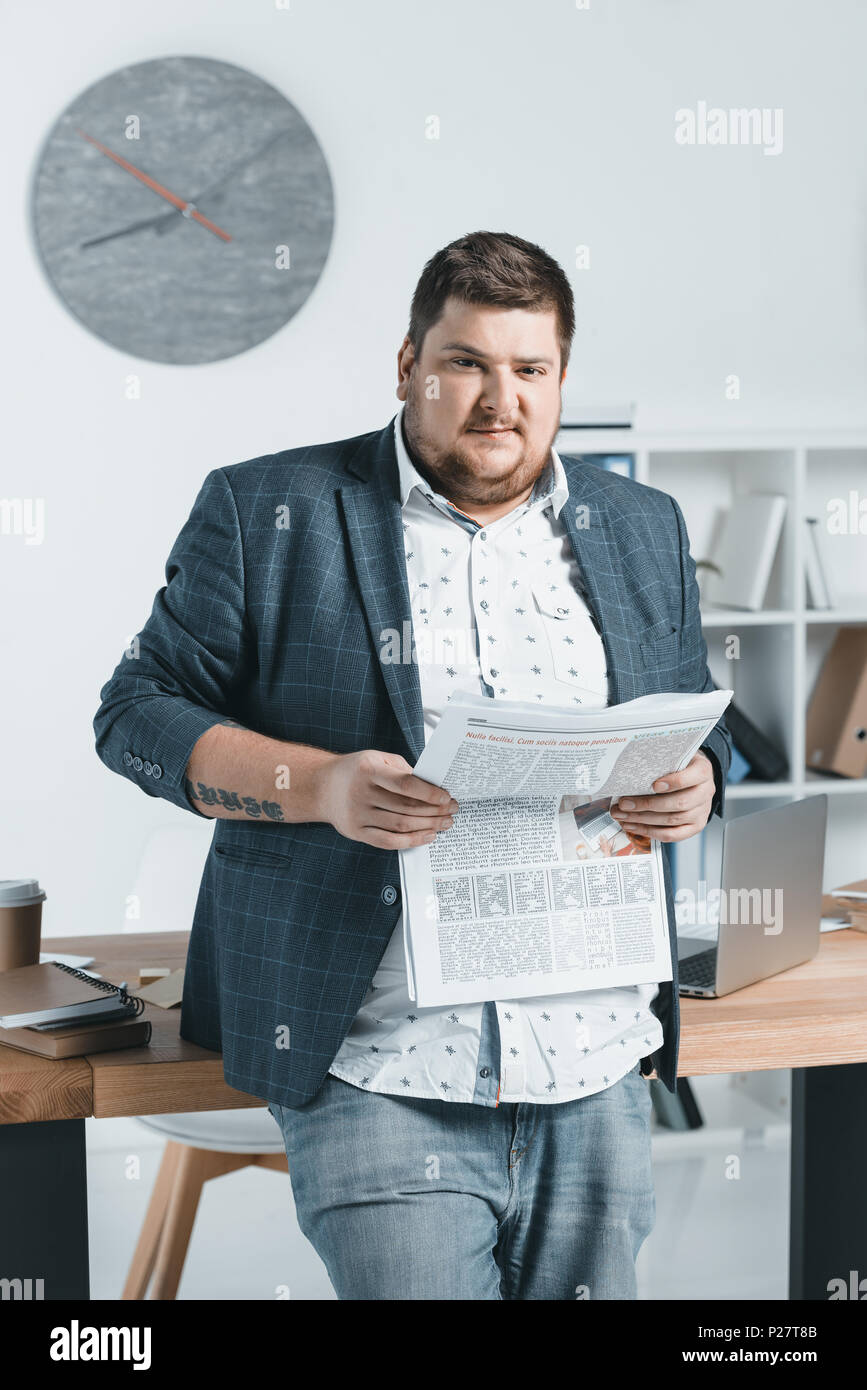 overweight businessman in suit reading newspaper at workplace Stock Photo