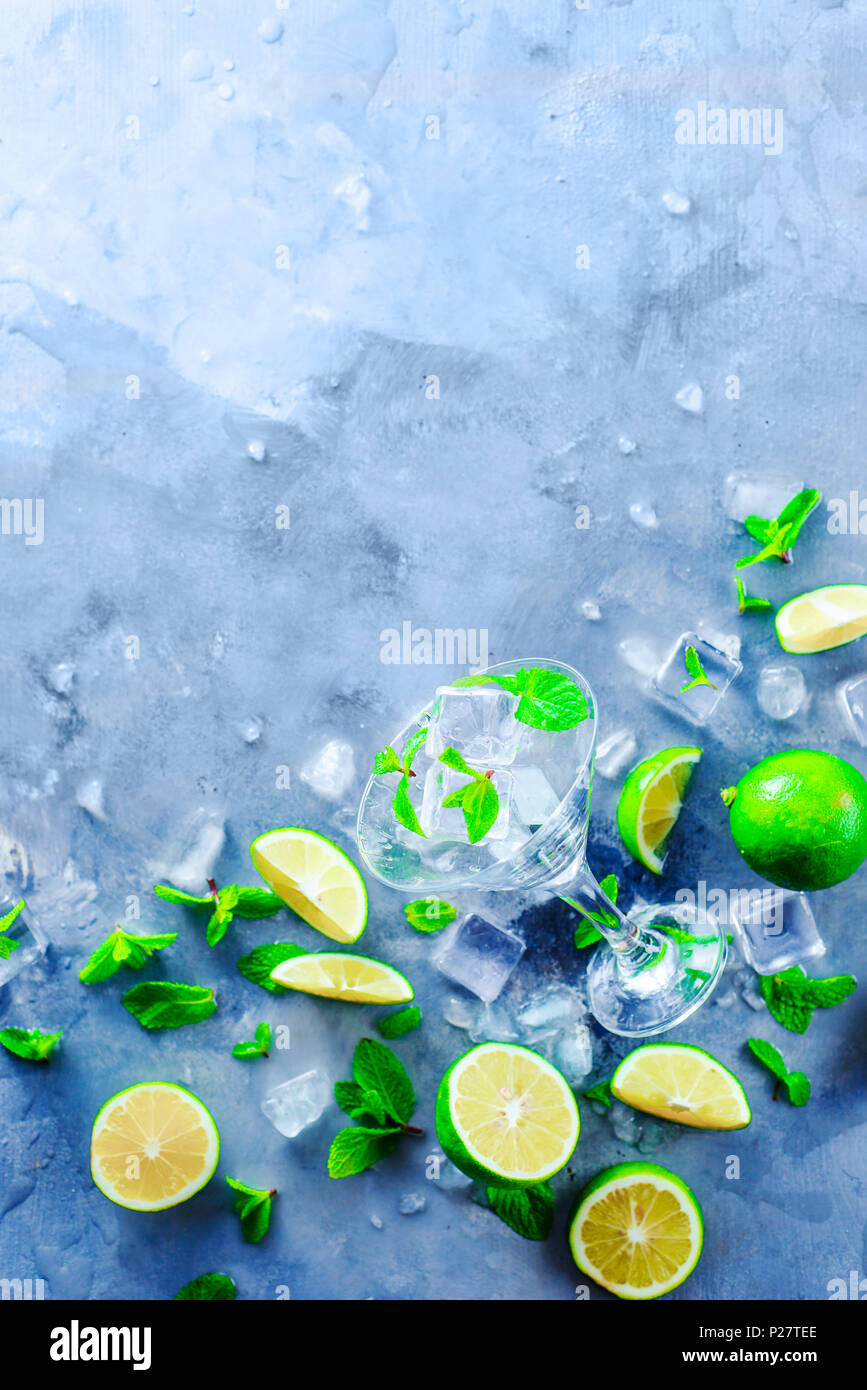Martini glass with mojito cocktail ingredients, mint, lime and ice cubes on a stone background. Summer refreshment flat lay. Preparing drinks concept  Stock Photo
