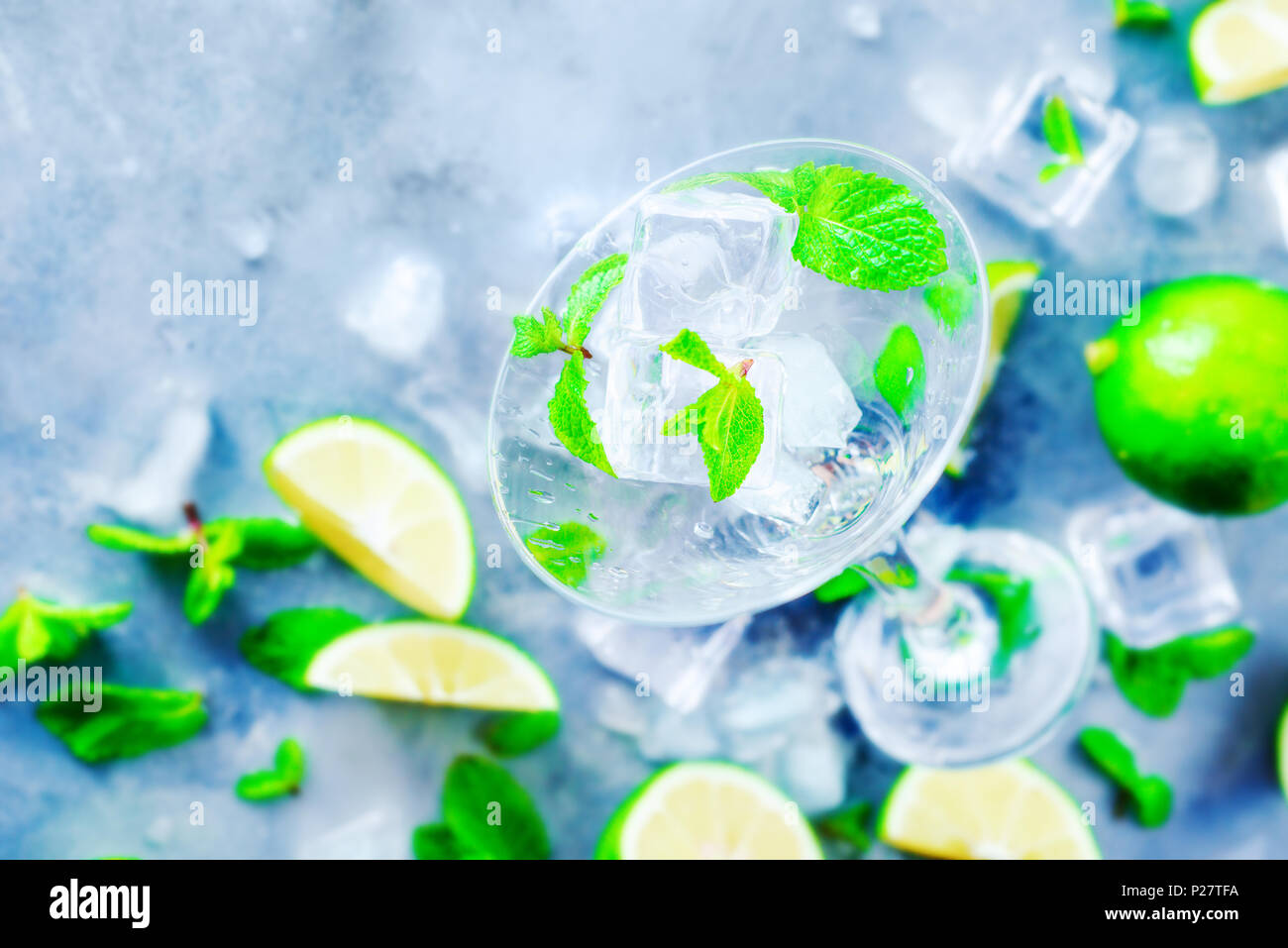Martini glass with mojito cocktail ingredients, mint, lime and ice cubes on a stone background. Summer refreshment flat lay. Preparing drinks concept  Stock Photo