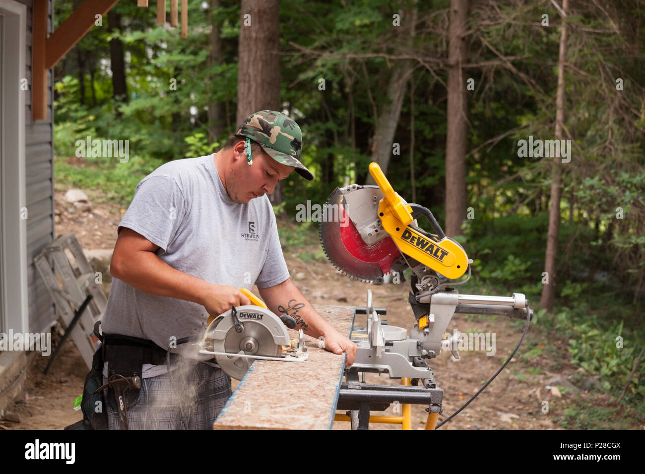 A construction worker using a handheld circular saw to cut a wooden plank. Stock Photo