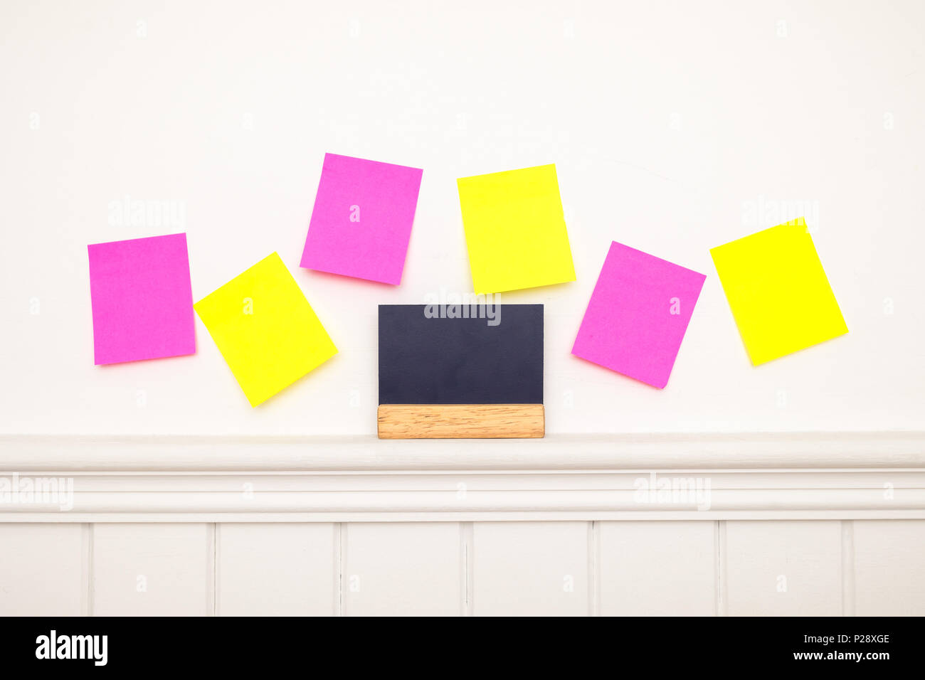 Empty colorful sticky notes and little blackboard on the wall . Stock Photo