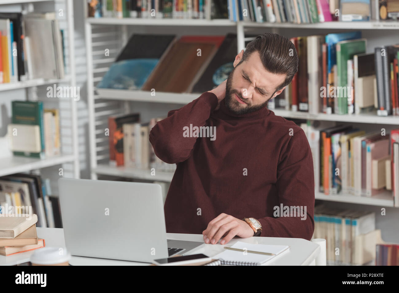 tired student touching neck while working with laptop in library Stock Photo