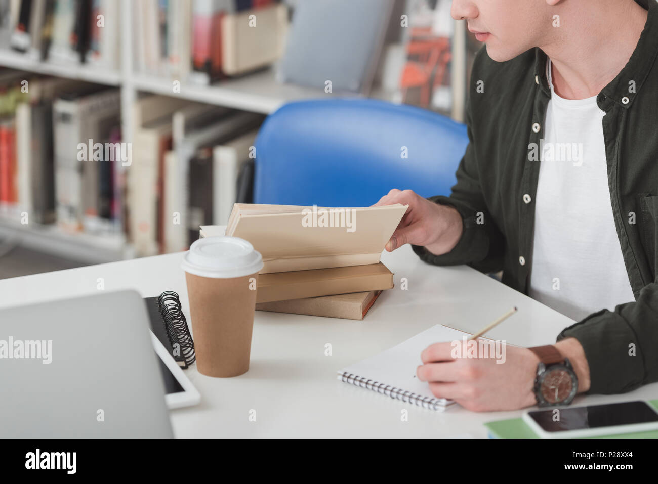 cropped image of student reading book and making notes in library Stock Photo