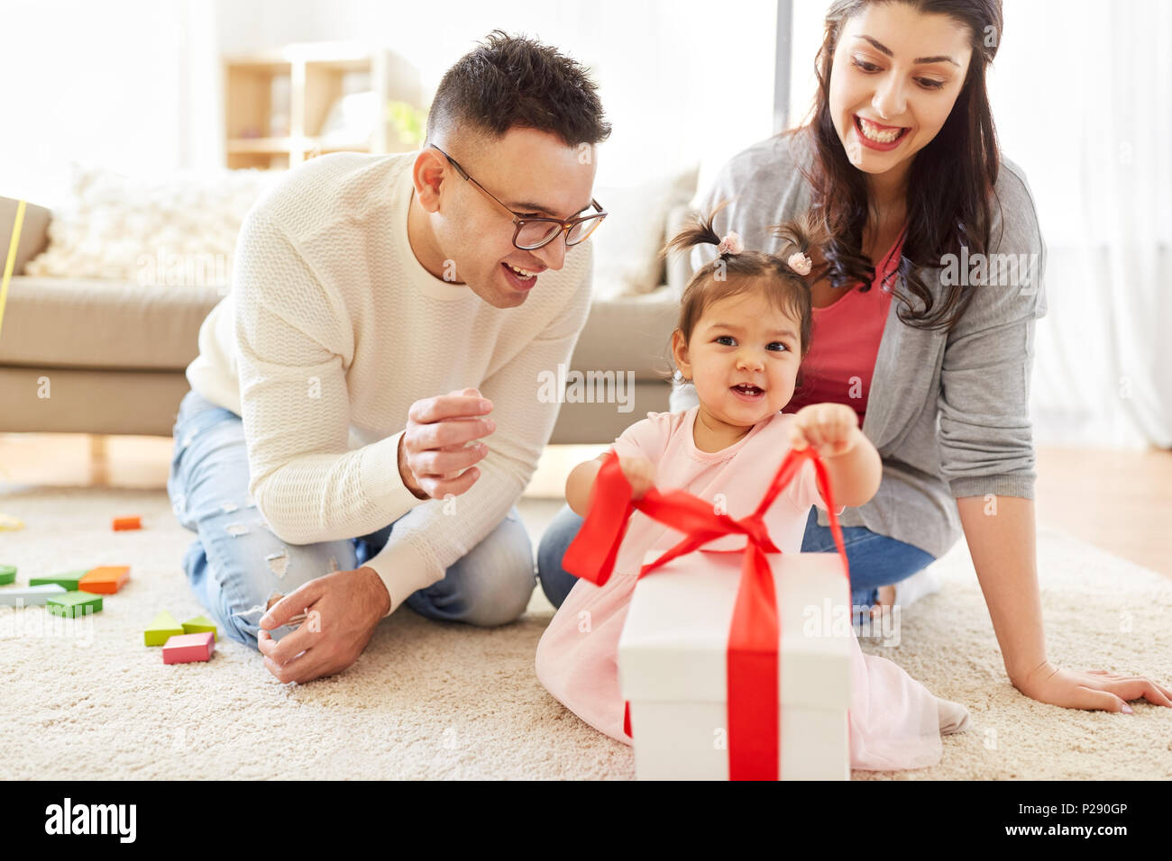 Baby Girl With Birthday Gift And Parents At Home Stock Photo