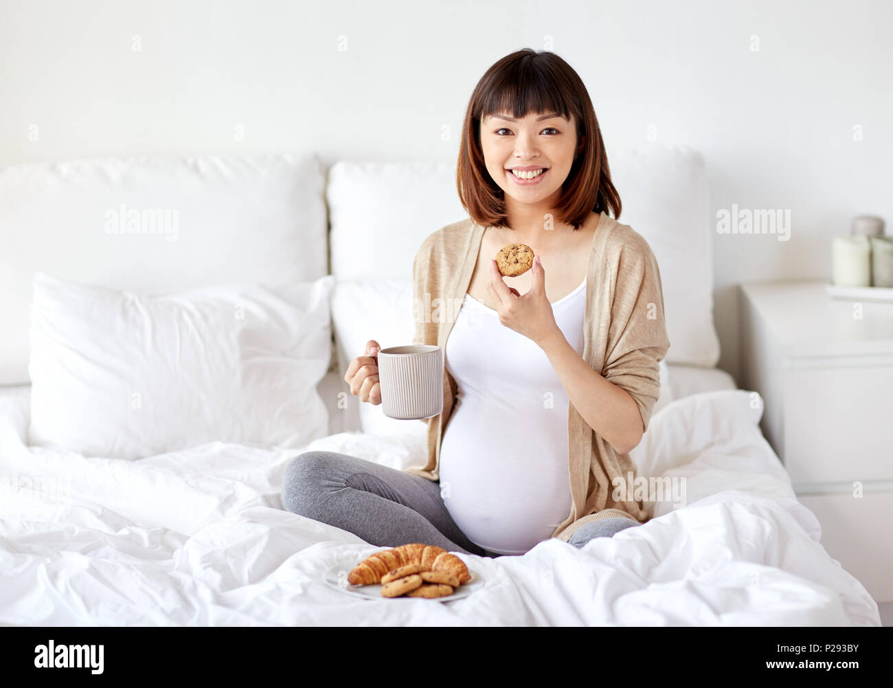 happy pregnant woman eating cookie in bed at home Stock Photo Alamy
