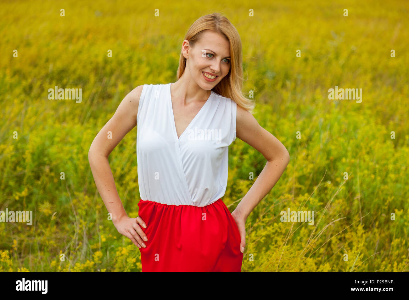 Smiling girl stands in a field of yellow flowers and poses in front of ...