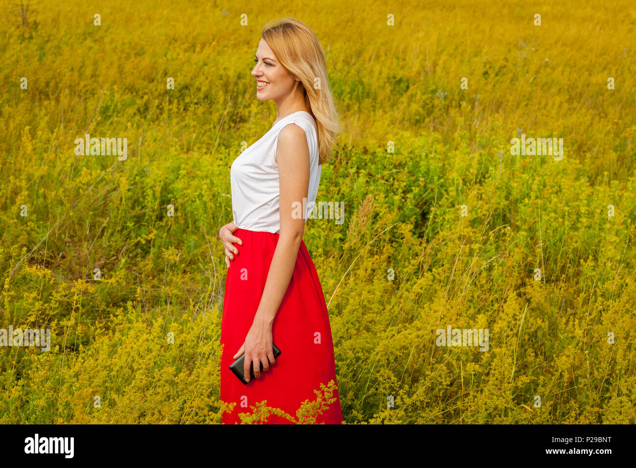 Smiling girl stands in a field of yellow flowers and poses in front of ...