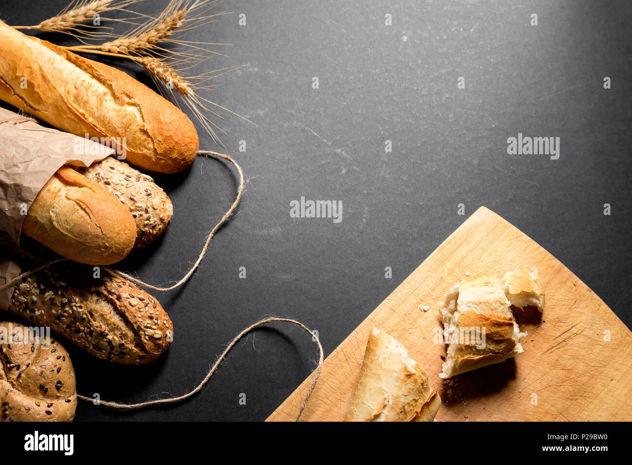 Different fresh bread with seeds and wooden bottom with crumbs, on black background. Useful as baker background Stock Photo