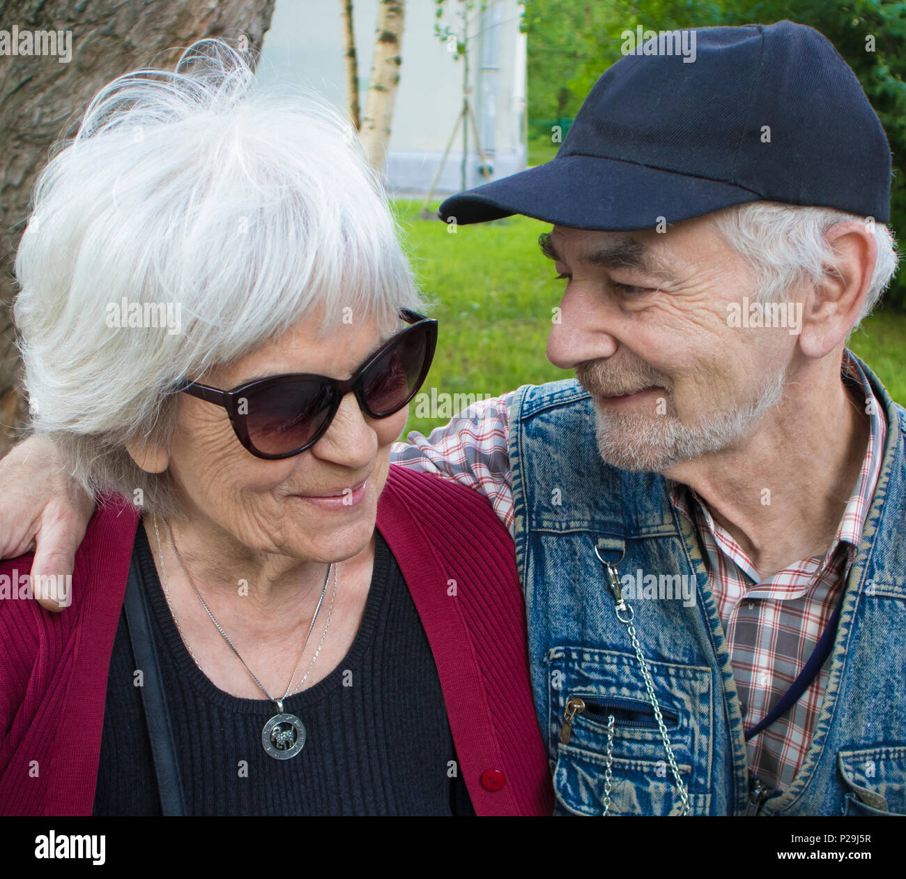 Happy elderly smiling couple sitting on the bench in the park, man looks at woman with love Stock Photo