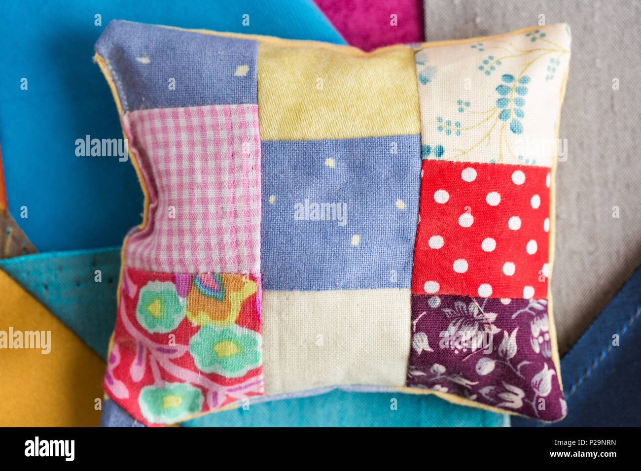 patchwork, quilting, sewing, tailoring and fashion concept - close-up beautiful colorful stitched cushion, macro on pillow with background of blue, gr Stock Photo
