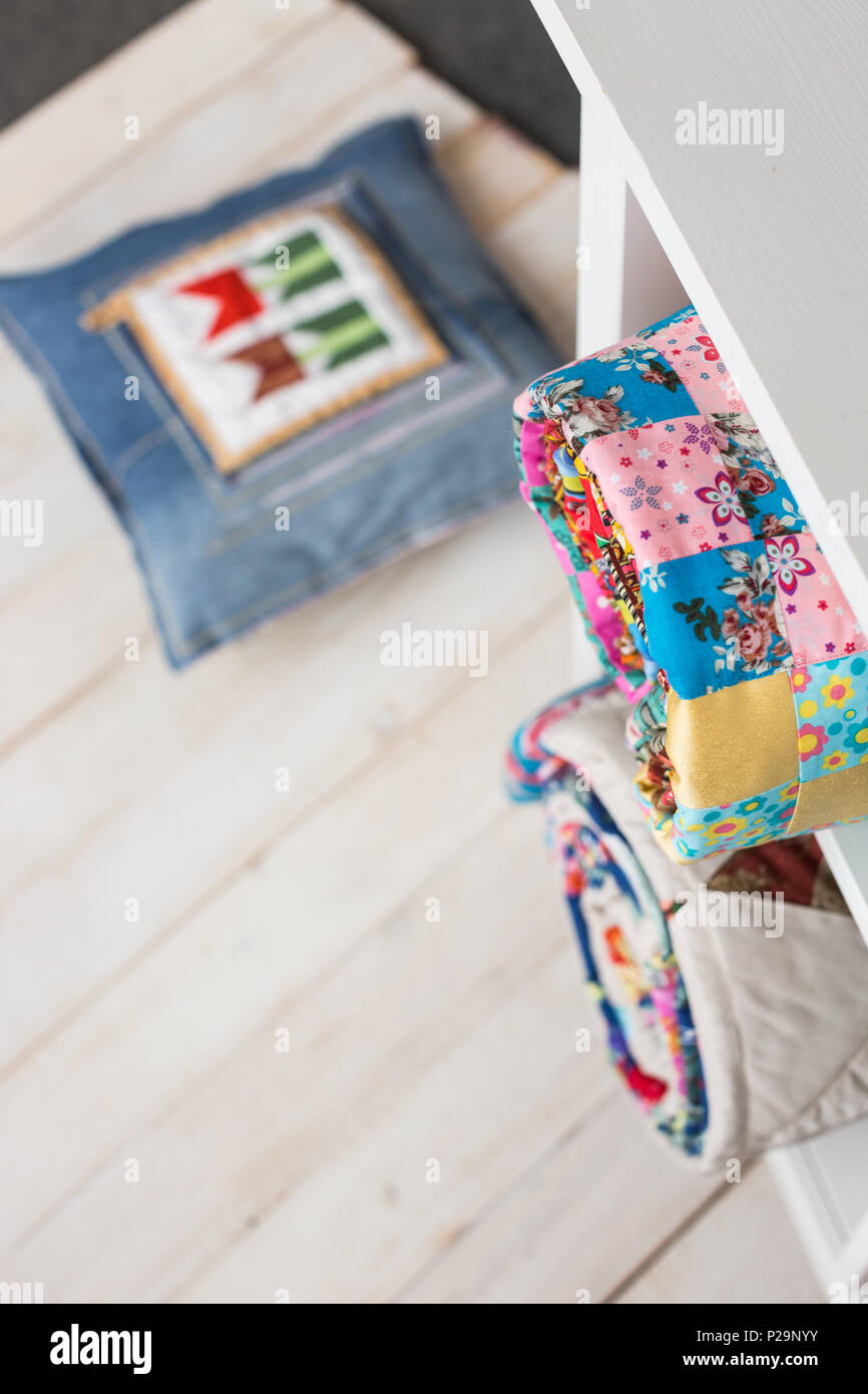 patchwork, sewing and fashion concept - two colorful quilted blankets at white shelves with few storage compartments in studio, pillow on floor in war Stock Photo