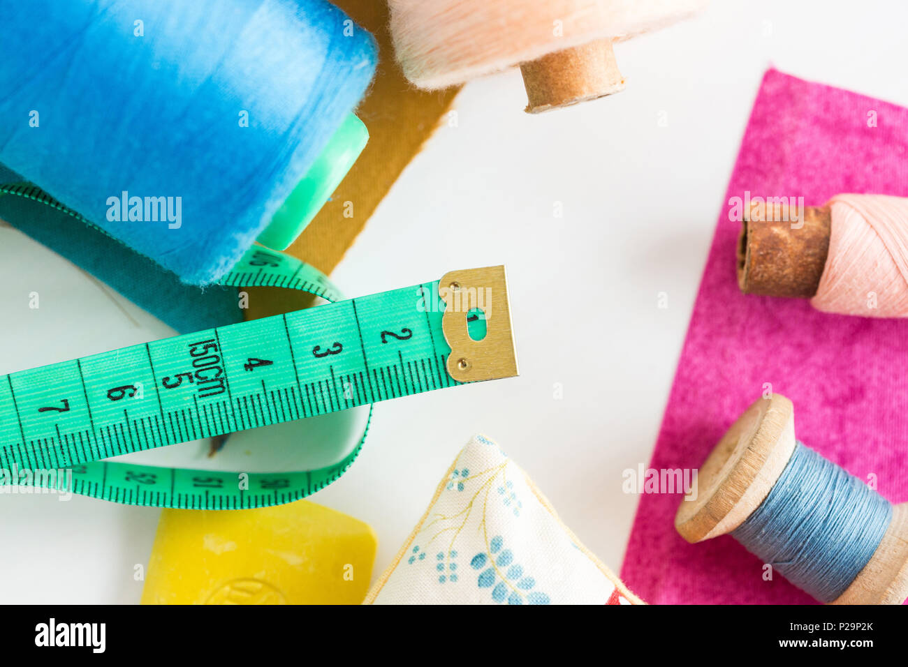 sewing, patchwork and tailoring concept - closeup on measuring meter, blue and pink threads in bobbins and purple and mustard color patches on white b Stock Photo