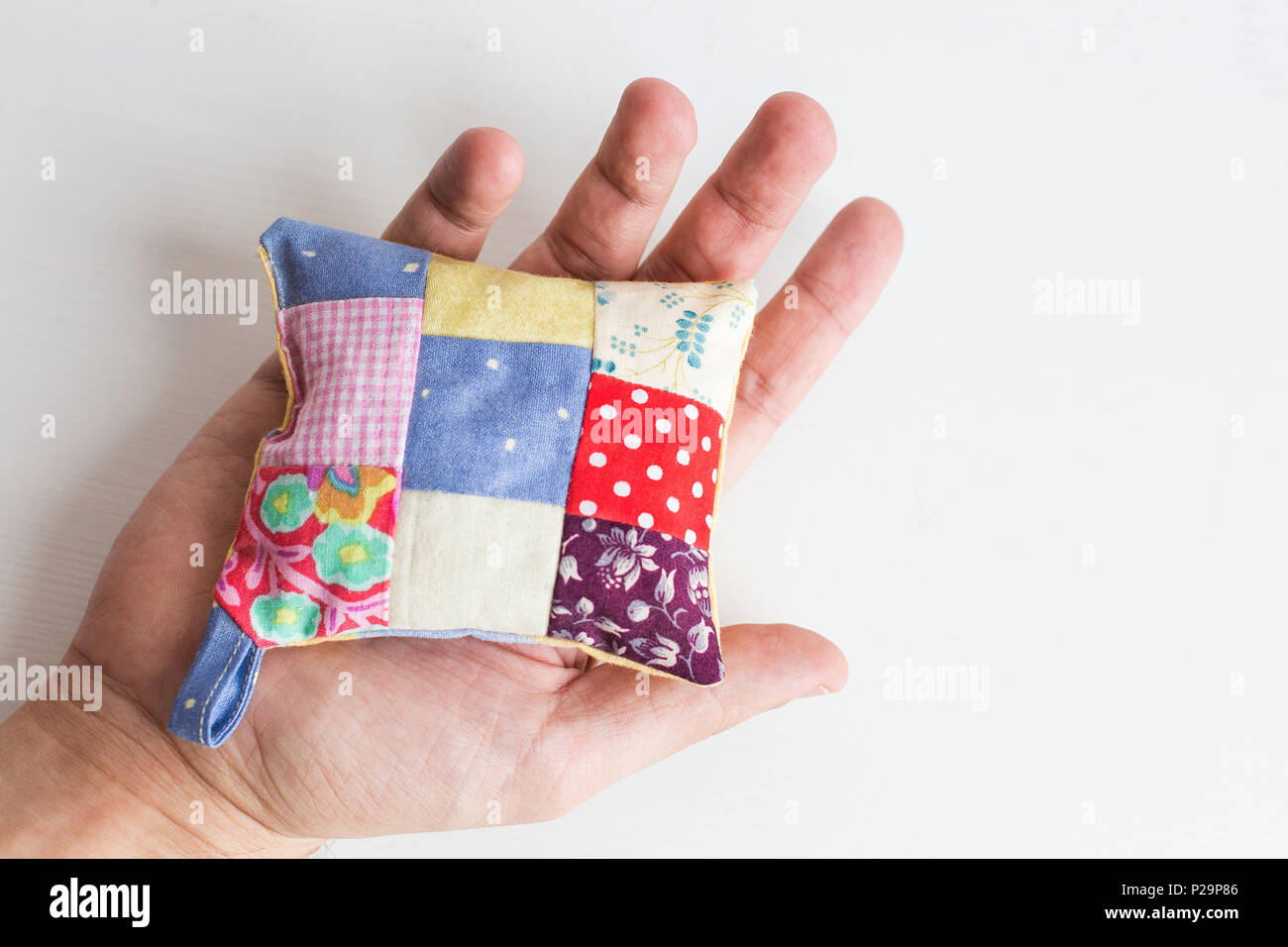 patchwork, quilting, sewing, tailoring and fashion concept - close-up on beautiful colorful stitched pincushion in human hand, macro on pillow with wh Stock Photo