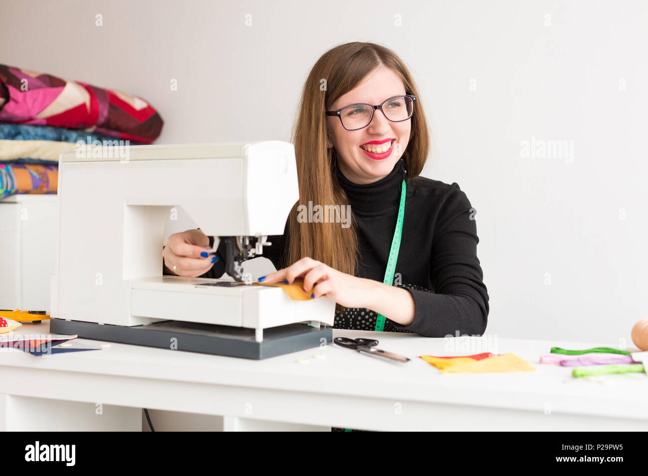 handcraft, workplace, lifestyle concept. in the workroom of sewing master decorated in light coloures there is a table with sewing machine, the young  Stock Photo