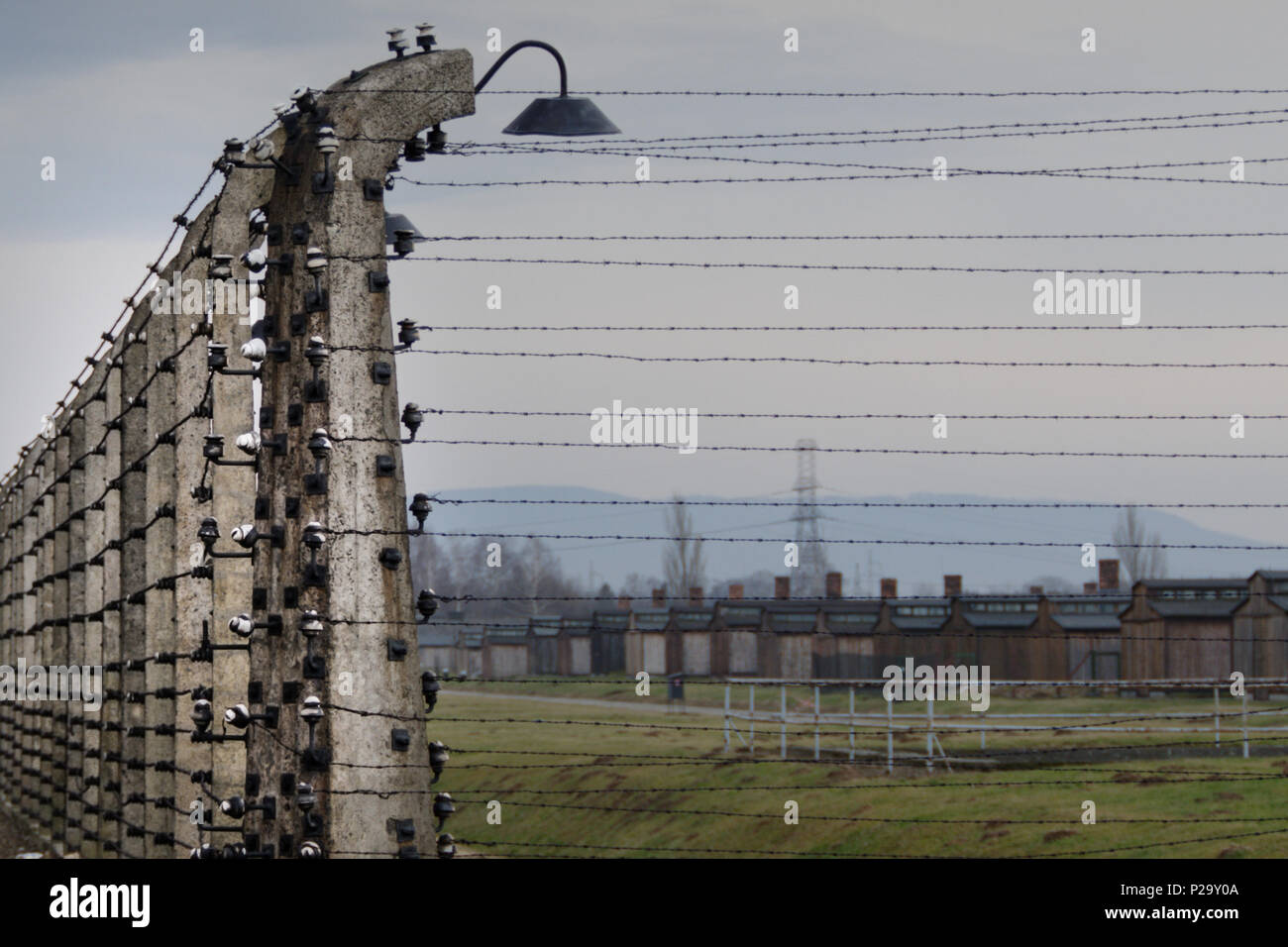 Electrified fence line in the ruins of Auschwitz-Birkenau with chimney stacks in the background. Stock Photo
