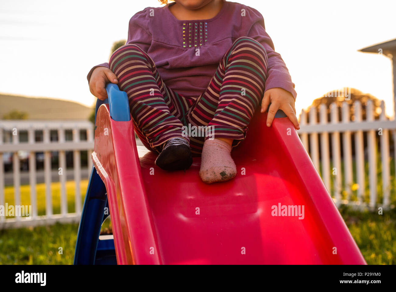 A little girl wearing striped pants and dancing on a slide. Stock Photo